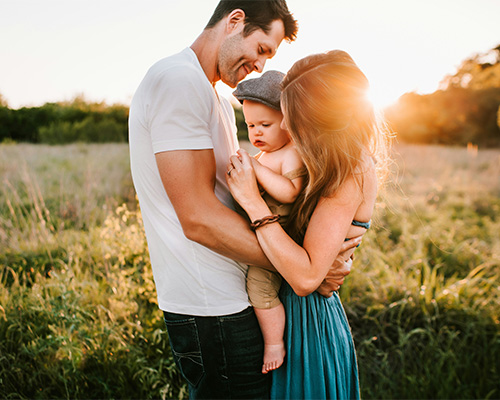 A Couple holding their baby in between them at sunset.